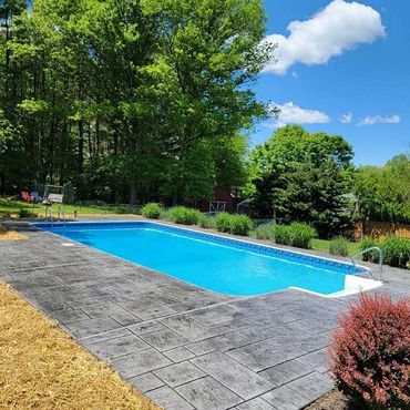 A serene outdoor swimming pool surrounded by lush greenery and clear blue skies.