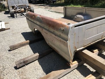 Rusty and weathered truck bed section resting on wooden planks outdoors.