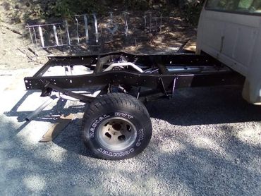 Partial vehicle chassis with a single tire and exhaust visible on gravel ground.