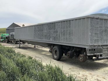 Large industrial trailer missing several wheels, parked on a rural dirt road.
