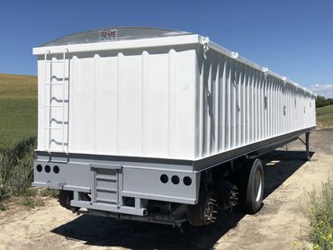 Large white and gray agricultural trailer with ladder and tarp on sunny day.