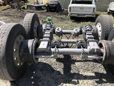 Heavy-duty truck axle assembly with dual wheels on a gravel surface.