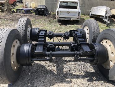 Newly painted truck axle assembly with wheels on gravel ground.