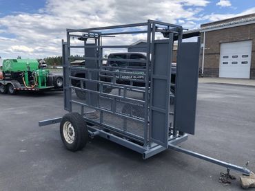 Metal livestock trailer with a single axle and mesh panels.