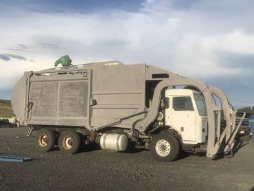 A large garbage truck parked on gravel under a cloudy sky.