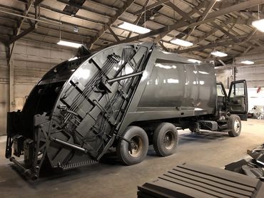 A large garbage truck inside a garage with its back open.