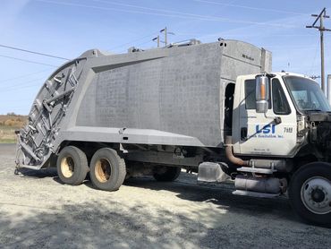 A large sanitation truck parked on a gravel surface under a clear sky.