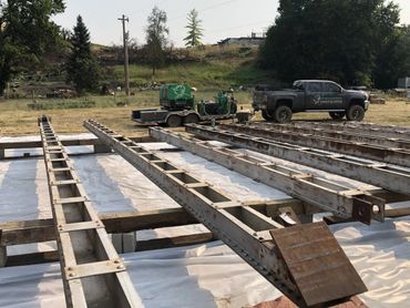 Steel beams laid out on a construction site with a truck and equipment in the background.