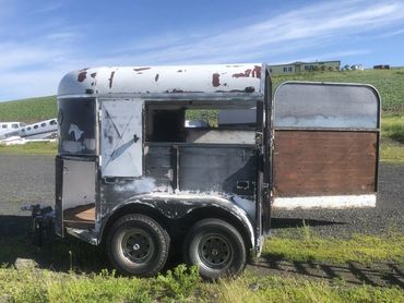 Old, weathered horse trailer with peeling paint and open door.