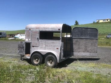 An old, weathered horse trailer with open doors in a rural area.