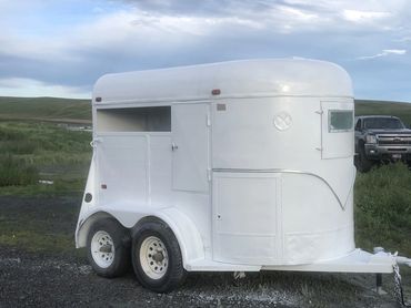 White horse trailer parked outdoors with a truck in the background.