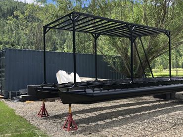 Black metal pontoon boat frame on stands outdoors.