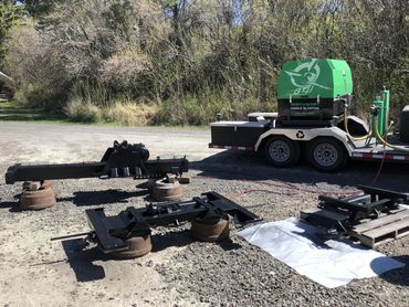 Industrial equipment parts laid out on gravel near a trailer in an outdoor setting.