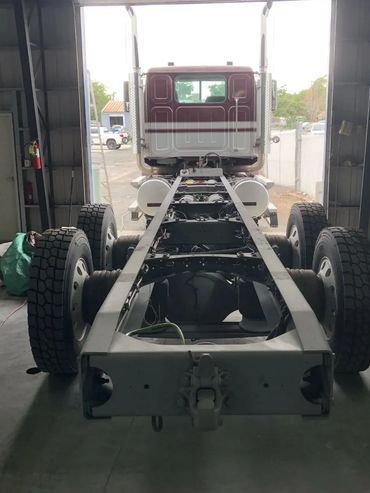 Rear view of a truck chassis inside a garage, showing large tires and exposed frame.