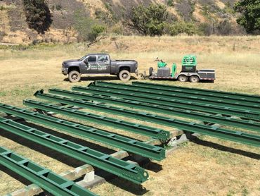 Pickup truck and trailer with green steel beams laid out on grass.