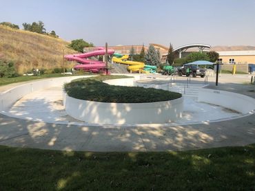 Empty outdoor pool with colorful water slides and greenery.
