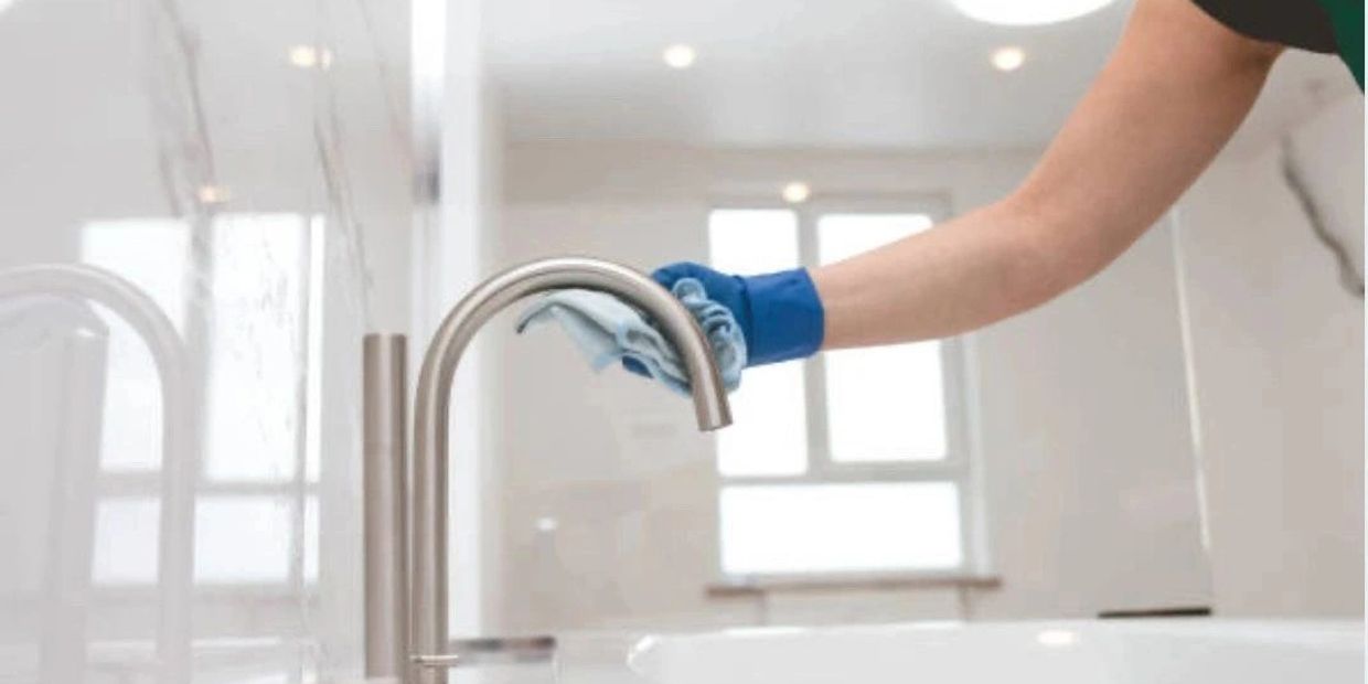 Person cleaning a modern bathroom faucet with a cloth and glove.