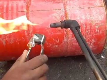Using a blowtorch to heat a red metal barrel outdoors.
