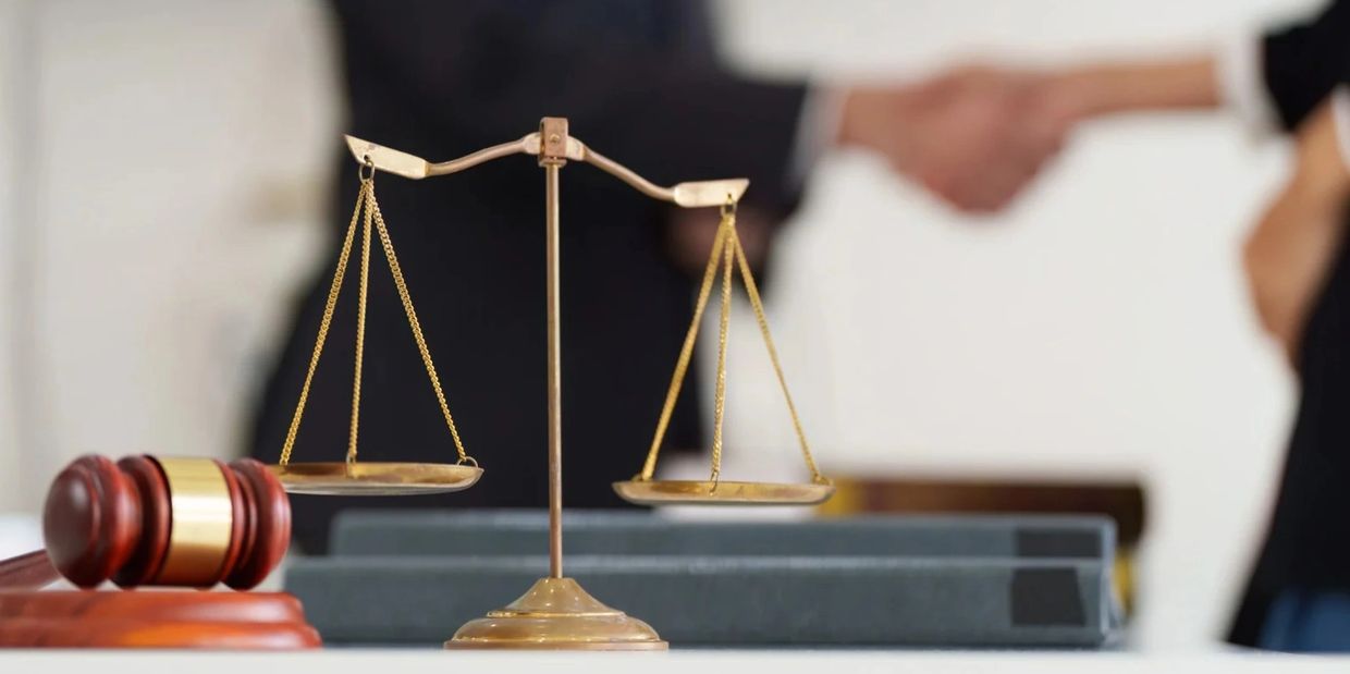 Scales of justice and gavel with handshake blurred in background.