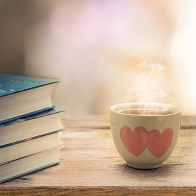 Stack of books on an outdoor table with a cup of hot tea.