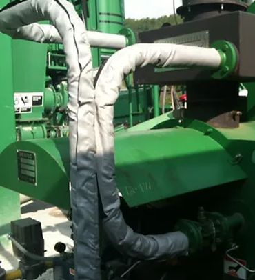 Insulated pipes connected to a green industrial machine outdoors.