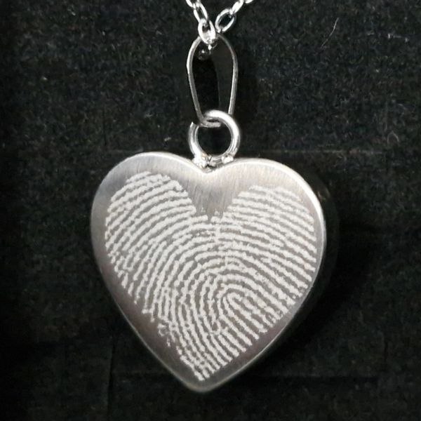 Heart-shaped pendant with fingerprint design on a chain.