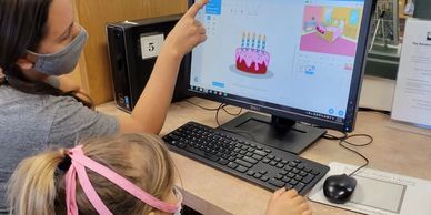 A photo from our Girls Who Code Class of a girl being taught how to code on a computer.