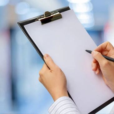Person holding a clipboard with a blank sheet and a pen.