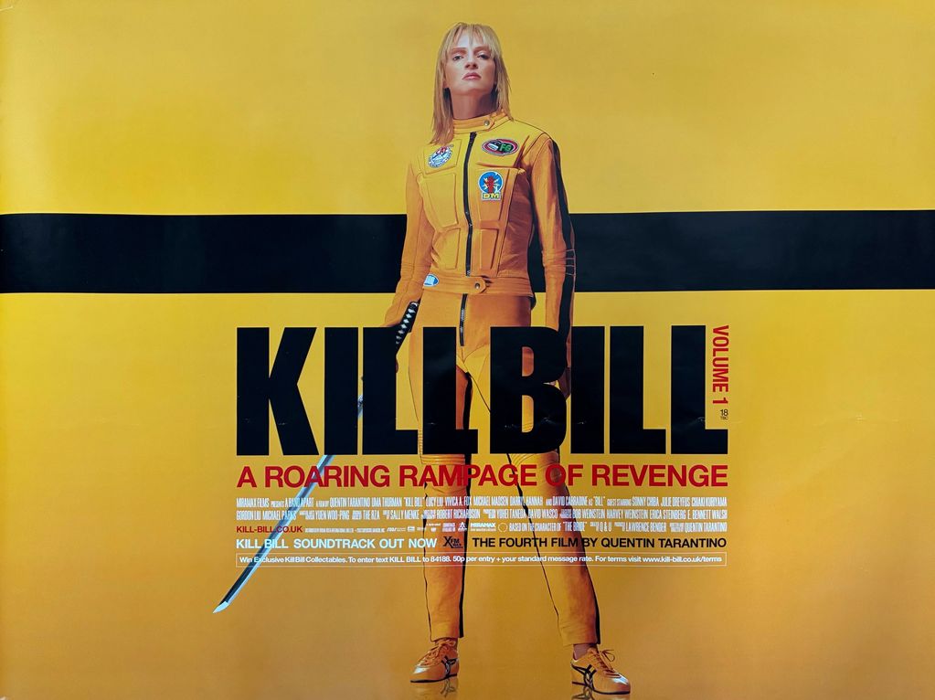 A woman wearing yellow leathers standing holding a samurai sword.