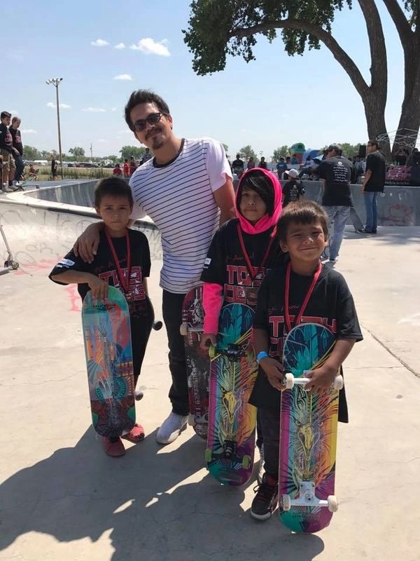 Man with three children holding colorful skateboards at a skate park.
