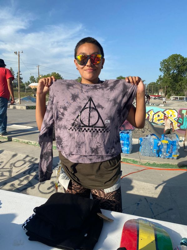 A person proudly holding up a tie-dye shirt outdoors on a sunny day.