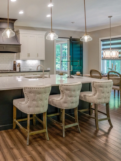Modern kitchen island with three upholstered bar stools and pendant lighting.