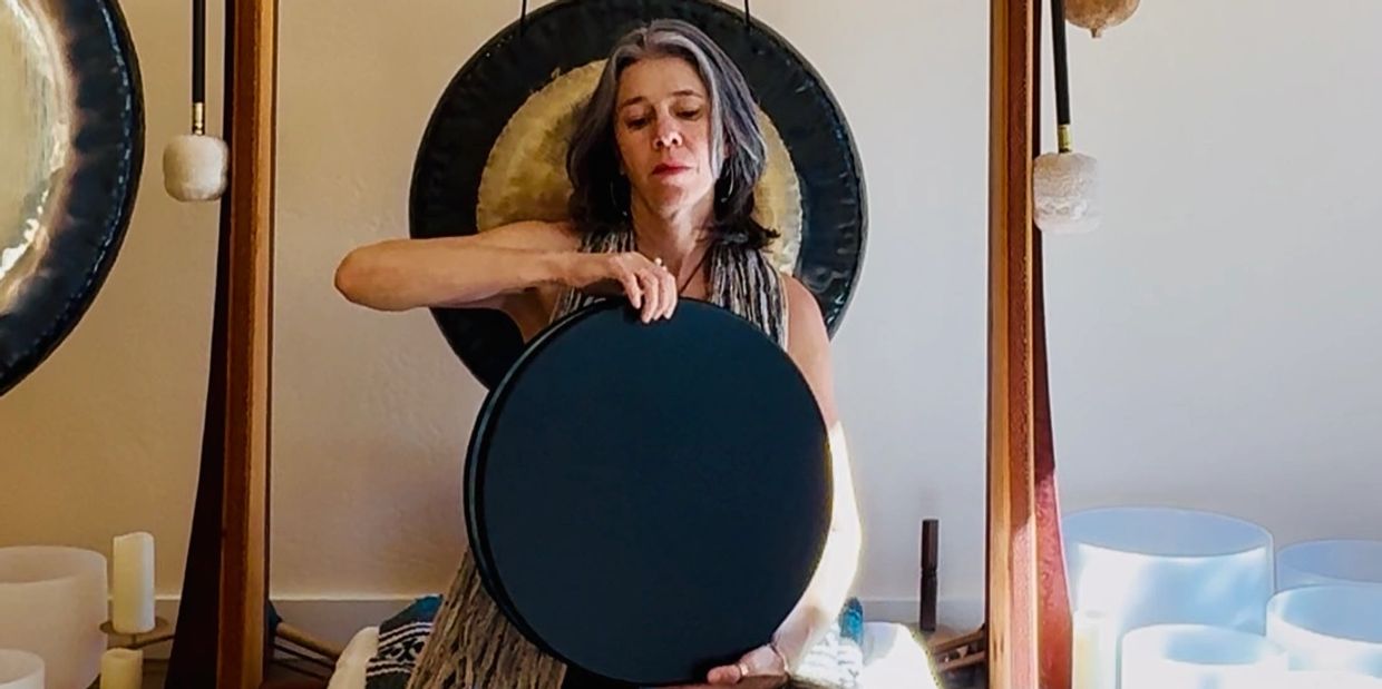 Woman playing a black handpan drum in a serene room.