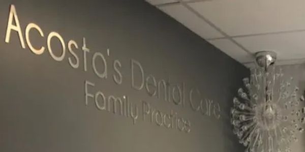 Sign for Acosta's Dental Care Family Practice on a dark wall.