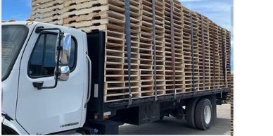 A truck loaded with a tall stack of wooden pallets.
