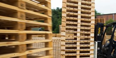 Stacks of wooden pallets arranged outdoors with a forklift nearby.