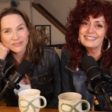Two women smiling in front of microphones with coffee mugs.
