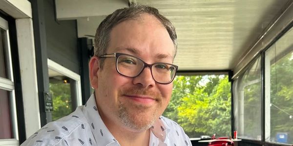 Smiling man wearing glasses and a white shirt.
