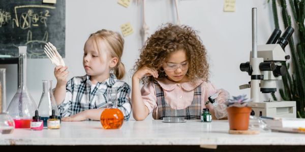 Two young girls engaged in a science experiment with lab equipment and microscope.