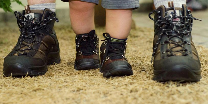 Matching hiking boots worn by an adult and a toddler standing side by side on a natural ground.