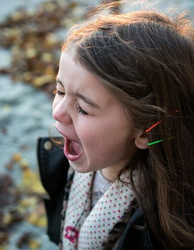 A young girl crying outdoors with her mouth wide open.