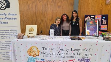 Three women standing behind a Tulare County League of Mexican American Women booth.