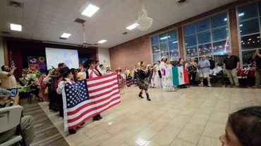 People in traditional attire hold U.S. and Mexican flags during a cultural event indoors.