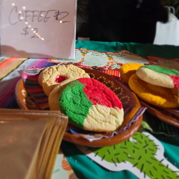 Colorful cookies and a sign showing prices for pan and coffee at a market stall.