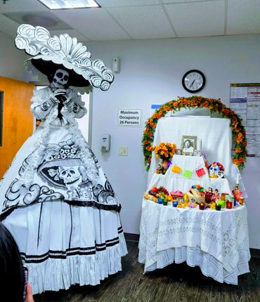 Person in Day of the Dead costume beside decorated altar.