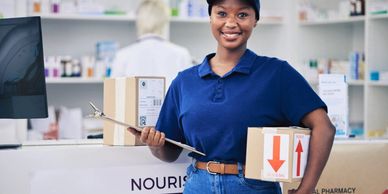 Smiling delivery woman holding packages and clipboard in a pharmacy.