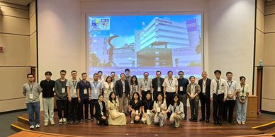 Group photo of 29 people in front of a presentation screen in an auditorium.