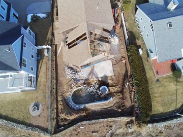 Aerial view of a house under construction with a small excavator in the backyard.