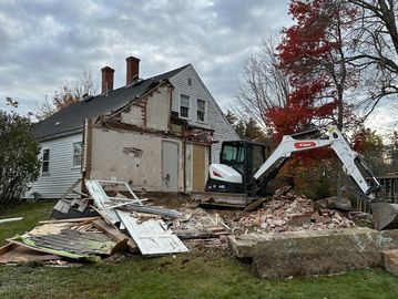 House demolition with excavator and debris scattered on the lawn.