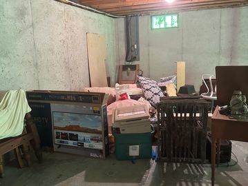 Cluttered basement with various stored items and exposed ceiling beams.